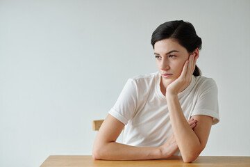 Portrait of pensive young woman leaning on desk and looking away