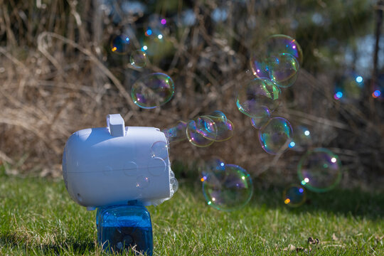 Portable soap bubble machine blowing colorful bubbles outdoors. Sunny day, selective focus.