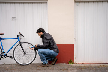 Fototapeta premium Man wearing jeans and black coat fixing a blue bike in front of garage