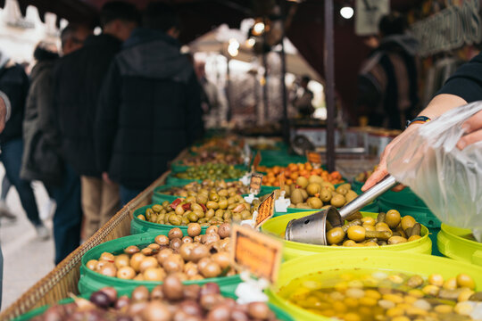 Hands of a shopkeeper scooping a handful of olives with gherkin at a Spanish medieval market street stall. - Powered by Adobe