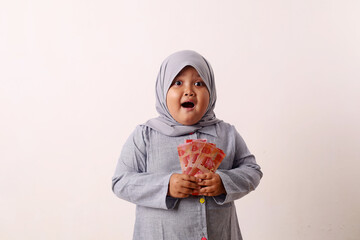 Surprised Asian muslim little girl standing while holding Indonesian banknotes. Eid Al-fitr concept