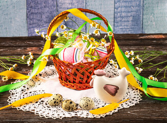 Easter composition with a basket with Easter eggs, decorative chicken, quail eggs on a wooden...