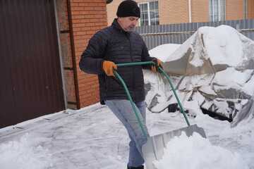 A man cleans snow in the winter in the courtyard of the house.