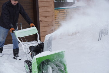 A man cleans snow in the winter in the courtyard of the house,  man cleaning snow with a snow blower