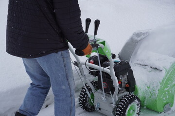 A man cleans snow in the winter in the courtyard of the house,  man cleaning snow with a snow blower