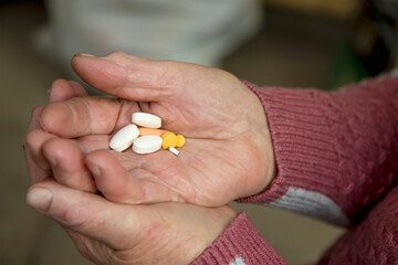 the hands of an elderly woman hold a handful of different pills to maintain health in old age