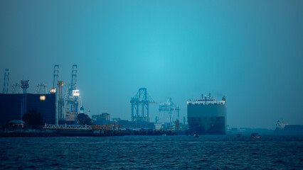 Large RoRo (Roll on/off) carrier vessels loading new cars and trucks at quayside into and out of the world market and commercial port, night scene blue tone process, sea front