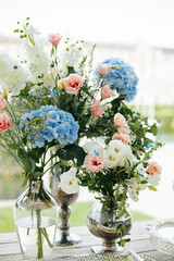 Composition of hydrangeas, eustoma and roses in vases against the backdrop of nature. 