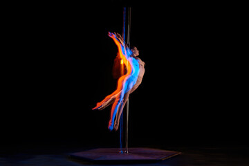Gymnastic tricks. Young girl performing pole dance isolated over black studio background with mixed neon lights. Concept of sport and dance, beauty of movements, action, modern style