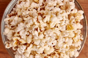 A bowl on a wooden background is completely filled with popcorn.