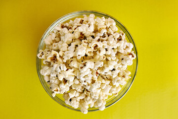 A bowl on a yellow background is completely filled with popcorn.