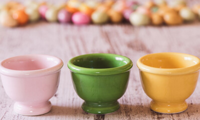 Three empty egg holders with small colored Easter eggs in the background