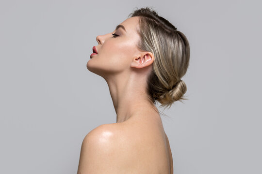 Young beautiful woman stands on her side with bare shoulders and back. Concept of hair and makeup, skin and body care