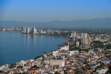 Fototapeta na wymiar Aerial panoramic view of Puerta Vallarta city scape with white houses and clay shingled roofs and Bay of Banderas, sunny day, blue sky.