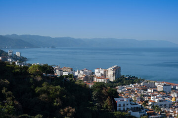 Aerial panoramic view of Puerta Vallarta city scape with white houses and clay shingled roofs and Bay of Banderas, sunny day, blue sky.