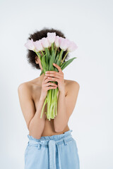 Shirtless african american woman holding tulips near face isolated on grey.