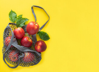 Mesh shopping gray bag with red apples on the yellow background.         Copy space. No plastic bag concept.