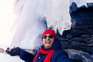 Adventure travel in winter, tourist man with red scarf makes selfie background ice grotto and cave,...