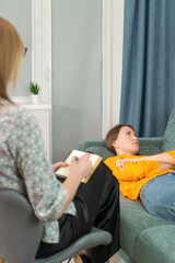 Young woman lying and resting on the couch with a psychologist sitting next to her and supporting...