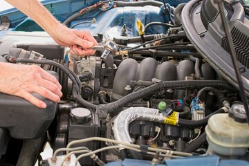 Automobile mechanic reaching into engine bay with socket wrench