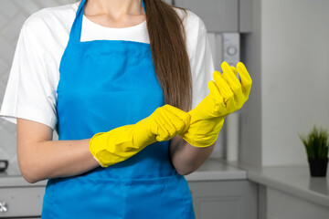 Close-up of women's hands wearing yellow rubber gloves. Woman in uniform is preparing to clean the apartment, copy space