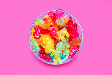 A large pile of multi-colored jelly marmalade candies in a glass bowl on a pink background. Variety...
