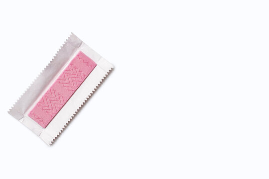 A pink piece of chewing gum in an unpacked wrapper on a white background. Flavored chewing gum is used after meals to freshen breath and clean teeth. The habit of chewing gum. Free space for text