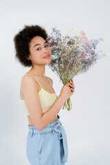 Young african american woman in top holding baby breath flowers and posing isolated on grey.