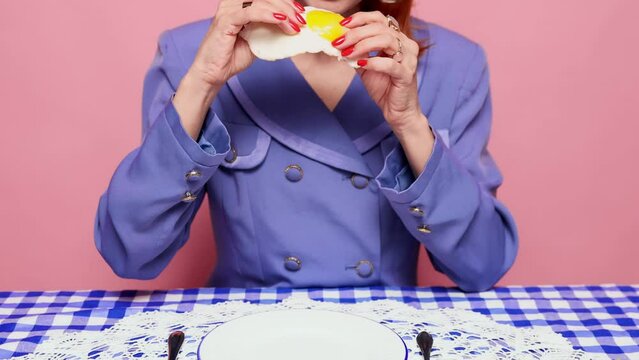 Feeling hungry. Food pop art photography. Young woman in stylish suit eating breakfast, fried egg with hands. Liquid yolk. Vintage, retro style. Complementary colors. Copy space for ad, text