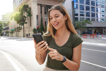 Beautiful smiling woman receiving good news on smartphone in modern metropolis