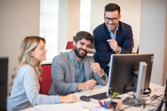 Group of three business people laughing together while looking at computer monitor and getting good company results.
