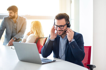 Smiling business man with headset working on laptop, talking to client, answering questions at...