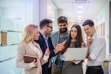 Obraz premium Team of five entrepreneurs standing and having a discussion using laptop computer on a meeting in office hallway.
