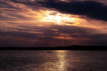 Silhouette of a man rowing at sunset. Dark forest at background. You can see the rays of sun between the dark clouds. Summer evening at lake.
