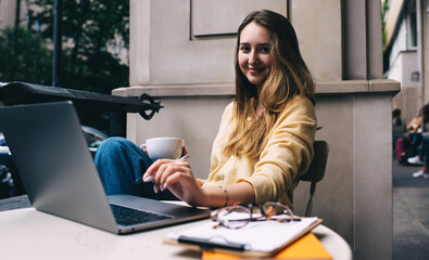 Attractive Caucasian woman sitting at table front open laptop computer while work distantly on freelance. Female student enjoying online educational courses on netbook. Shopping on website