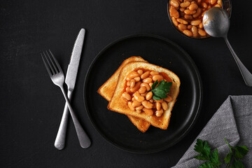 Toast bread with baked beans with parsley on plate on black table. top view