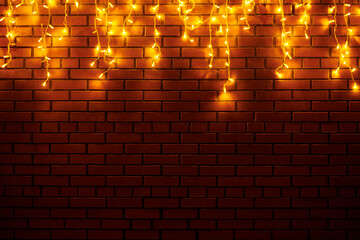 Yellow lights garlands hanging from red brick wall at evening, beautiful christmas house decoration with magic holiday atmosphere. Festive Christmas garlands with luminous yellow light on wall