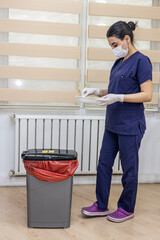 Nurse throws medical garbage into Medical waste bin in office. A female nurse holding a red garbage bag. Maid and infection trash in hospital. Infectious control.