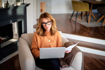 Mid aged woman sitting at home and using laptop for work