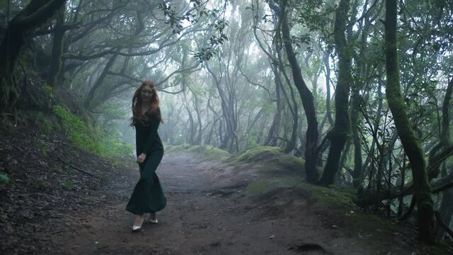 Beautiful woman in an elf costume is walking in a magic green enchanted forest.