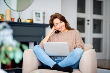 Smiling caucasian woman sitting in an armchair at home and using laptop