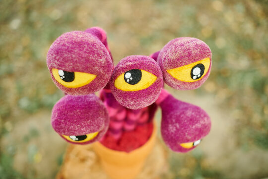 Purple striped flower with yellow eyes in clay pot on tree stump, strange crazy art object in outdoor art exhibition. Surreal big eyed flower in pot outdoor background, crazy mad weird art object