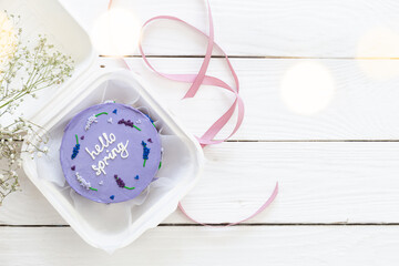 Fototapeta na wymiar Plastic lunchbox with delicious bento cake Hello spring on white wooden background, copy space.