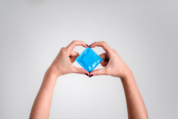 Una mujer sostiene un preservativo mientras forma un corazón con sus manos. Protección contra...