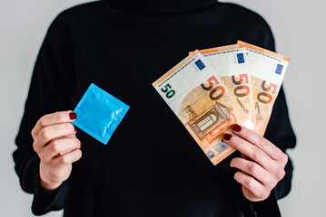 Una mujer sostiene un preservativo con una mano y tres billetes de cincuenta euros con la otra...