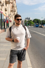 A man walks down a city street with a cup of coffee