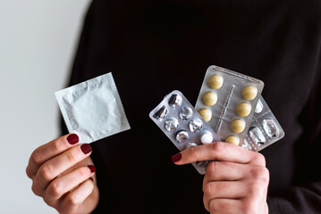 Una mujer sostiene un preservativo con una mano y tres blísters de pastillas con la otra mano....
