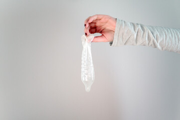 Una mano femenina sostiene un preservativo de látex usado, sobre fondo blanco. Concepto de sexo...