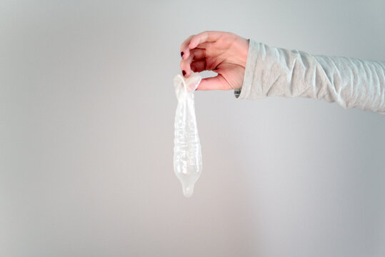 Una mano femenina sostiene un preservativo de l&aacute;tex usado, sobre fondo blanco. Concepto de sexo seguro. M&eacute;todo anticonceptivo. Prevenci&oacute;n de enfermedades de transmisi&oacute;n sexual.