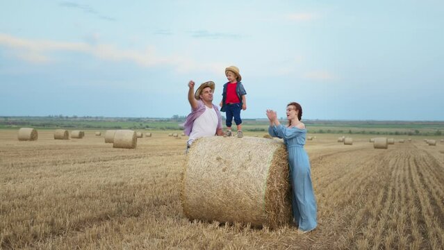 happy family with male child standing on a haystack launch paper plane and clap their hands